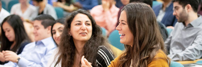 Two young women smiling and chatting in a large lecture hall