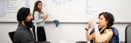 Learners in discussion in front of a whiteboard filled with notes