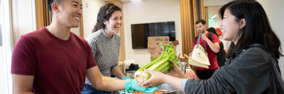 A worker at the Student Food Markey hands a bunch of celery to a student